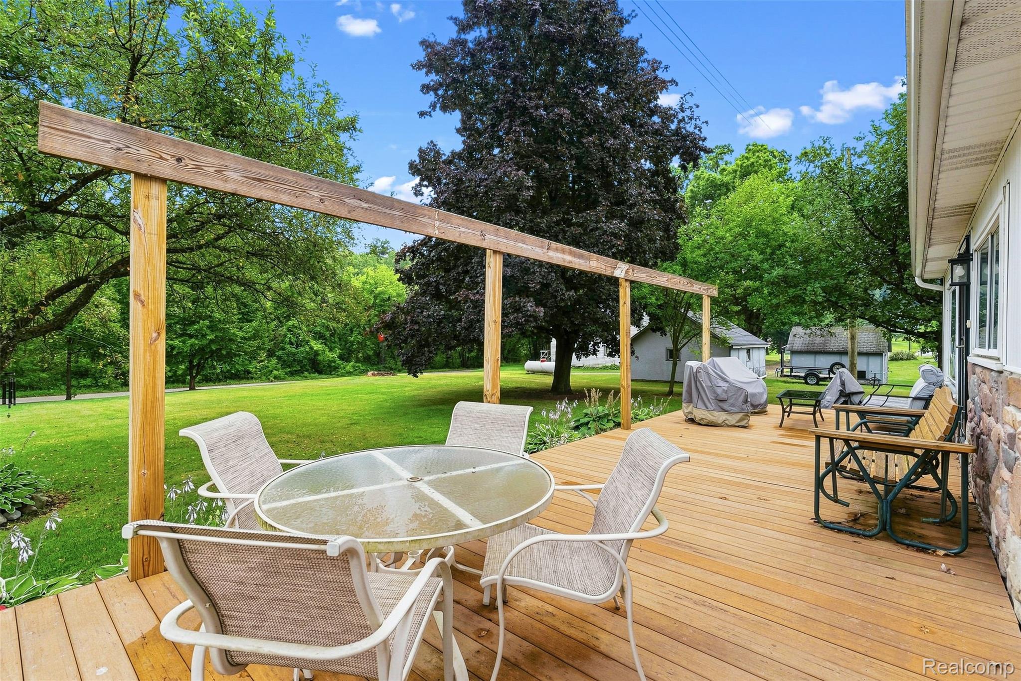 3319 Valentine Road Lapeer, MI 48446 - Photo 36 of 39 Expansive wood deck with a partial pergola structure, stone veneer exterior, and a lush green lawn