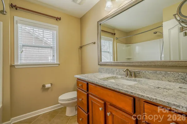 a bathroom with a granite countertop toilet a sink a mirror and a window