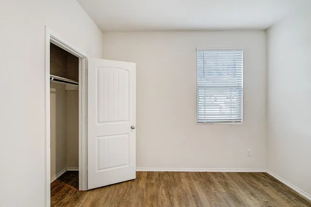 an empty room with wooden floor closet and windows