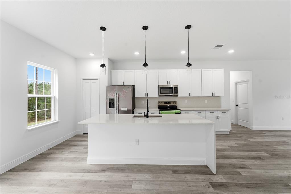 6312 Southwest 144th Lane Road Ocala, FL 34473 - Photo 8 of 32 a large white kitchen with kitchen island a stove a sink a refrigerator and white cabinets with wooden floor