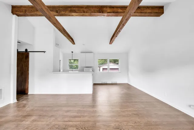 a view of a hallway to an empty room with wooden floor and windows