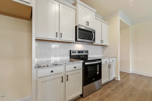 a kitchen with stainless steel appliances granite countertop white cabinets a sink a stove a microwave and cabinetry