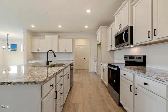 a kitchen with stainless steel appliances granite countertop a sink stove oven a refrigerator with white cabinets and wooden floor