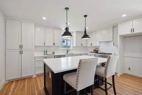 a kitchen that has a sink a microwave oven a stove and white cabinets with wooden floor