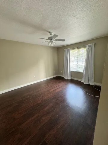 an empty room with wooden floor fan and windows