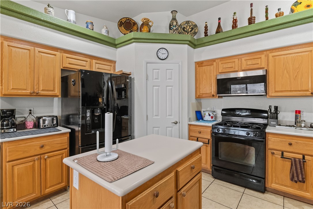 2516 Morrow Ridge Place Laughlin, NV 89029 - Photo 21 of 93 Kitchen with black appliances, light countertops, light tile patterned floors, a center island, and wood finish cabinets
