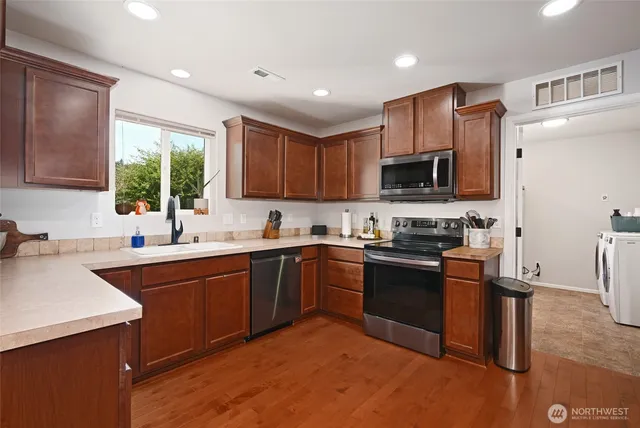 a kitchen with stainless steel appliances granite countertop a sink dishwasher stove top oven and wooden cabinets