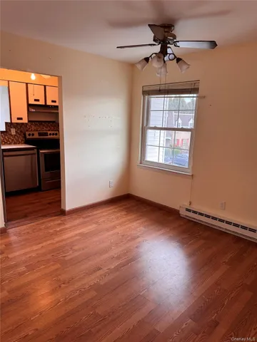 an empty room with wooden floor kitchen view and windows