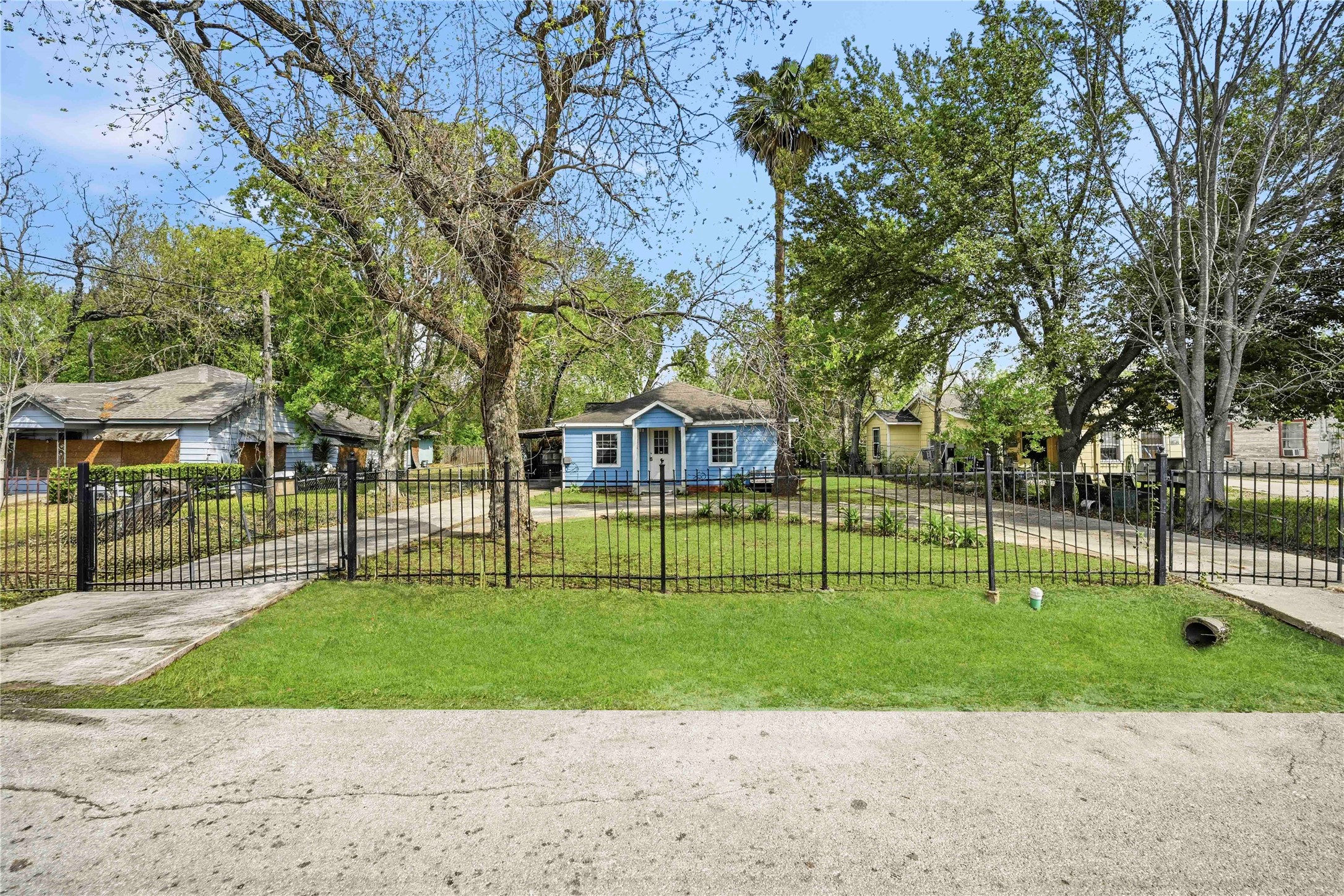 5513 Makeig Street Houston, TX 77026 - Photo 3 of 33 Charming single-story house with a welcoming front yard, enclosed by a black iron fence. Surrounded by mature trees, it offers a serene suburban feel with neighboring homes visible. Ideal for those seeking a cozy, peaceful setting.
