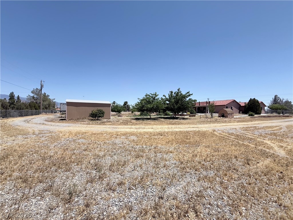 1220 East Gamebird Road Pahrump, NV 89048 - Photo 23 of 49 A spacious, open parcel with distant structures and mature trees under a clear sky.