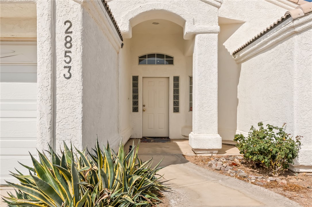 2853 Winchester Road Bullhead City, AZ 86442 - Photo 3 of 40 The property features a stucco exterior, a covered entryway with an arched ceiling, and a white front door with decorative glass block sidelights