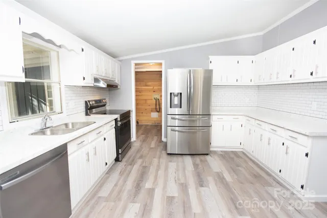 a kitchen with granite countertop a refrigerator a sink dishwasher and white cabinets with wooden floor