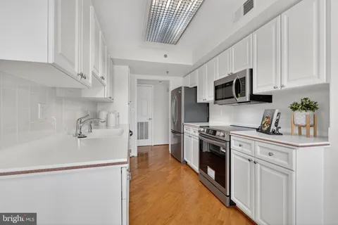 a kitchen with stainless steel appliances granite countertop a refrigerator a stove top oven a sink dishwasher and white cabinets with wooden floor