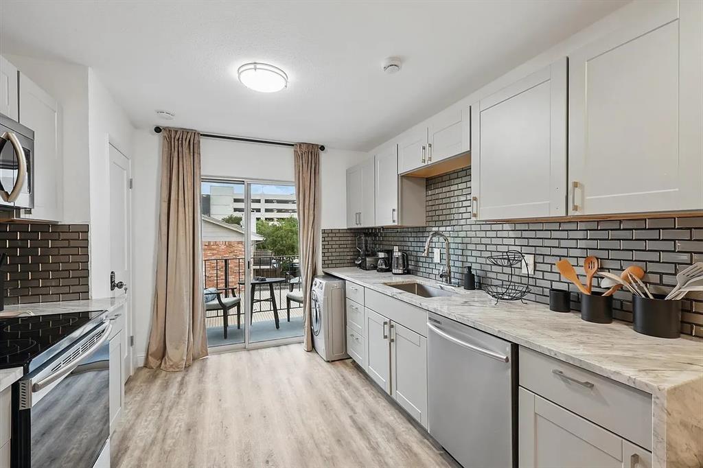 8083 Meadow Road, Unit 265 Dallas, TX 75231 - Photo 4 of 22 Kitchen featuring appliances with stainless steel finishes, light stone countertops, light wood finished floors, washer / clothes dryer, and white cabinetry