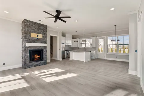 a view of a livingroom with a fireplace a ceiling fan and a kitchen view