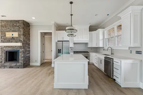 a kitchen with stainless steel appliances granite countertop a stove a sink dishwasher a refrigerator white cabinets and wooden floor