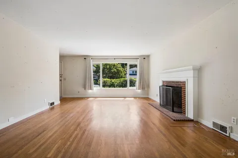 an empty room with wooden floor fireplace and windows