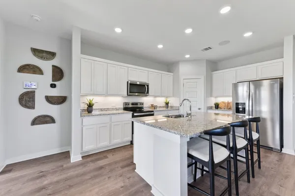 a kitchen with stainless steel appliances granite countertop a sink a stove a refrigerator cabinets and a dining table with wooden floor