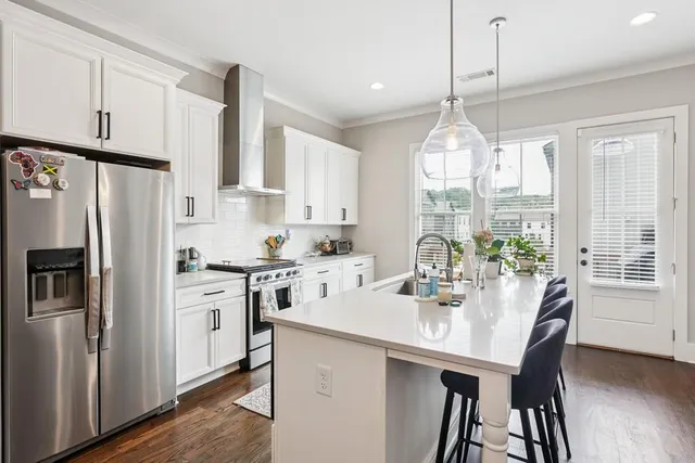 a kitchen with stainless steel appliances granite countertop a refrigerator a sink dishwasher a stove a dining table and chairs with wooden floor