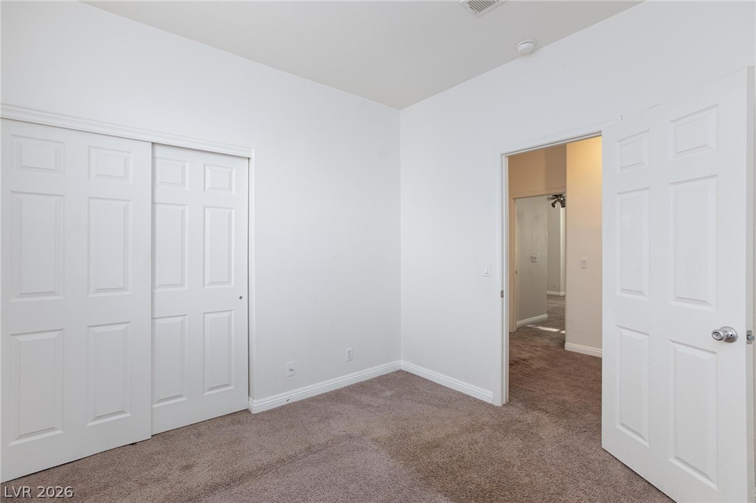 2246 Ramsgate Drive Henderson, NV 89074 - Photo 18 of 36 A well-lit bedroom features plush carpeting and convenient bi-fold closet doors, with an adjoining hallway visible.