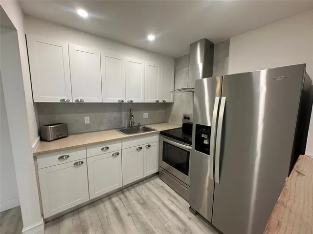 a kitchen with stainless steel appliances granite countertop a refrigerator a sink and white cabinets