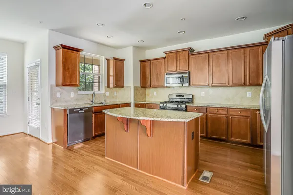 a kitchen with stainless steel appliances granite countertop a stove a sink dishwasher and a refrigerator with wooden floor
