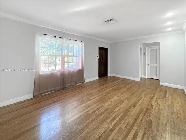 a view of an empty room with wooden floor and a window