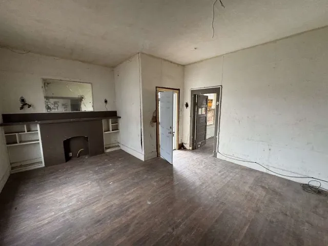 a view of an empty room with wooden floor and a fireplace