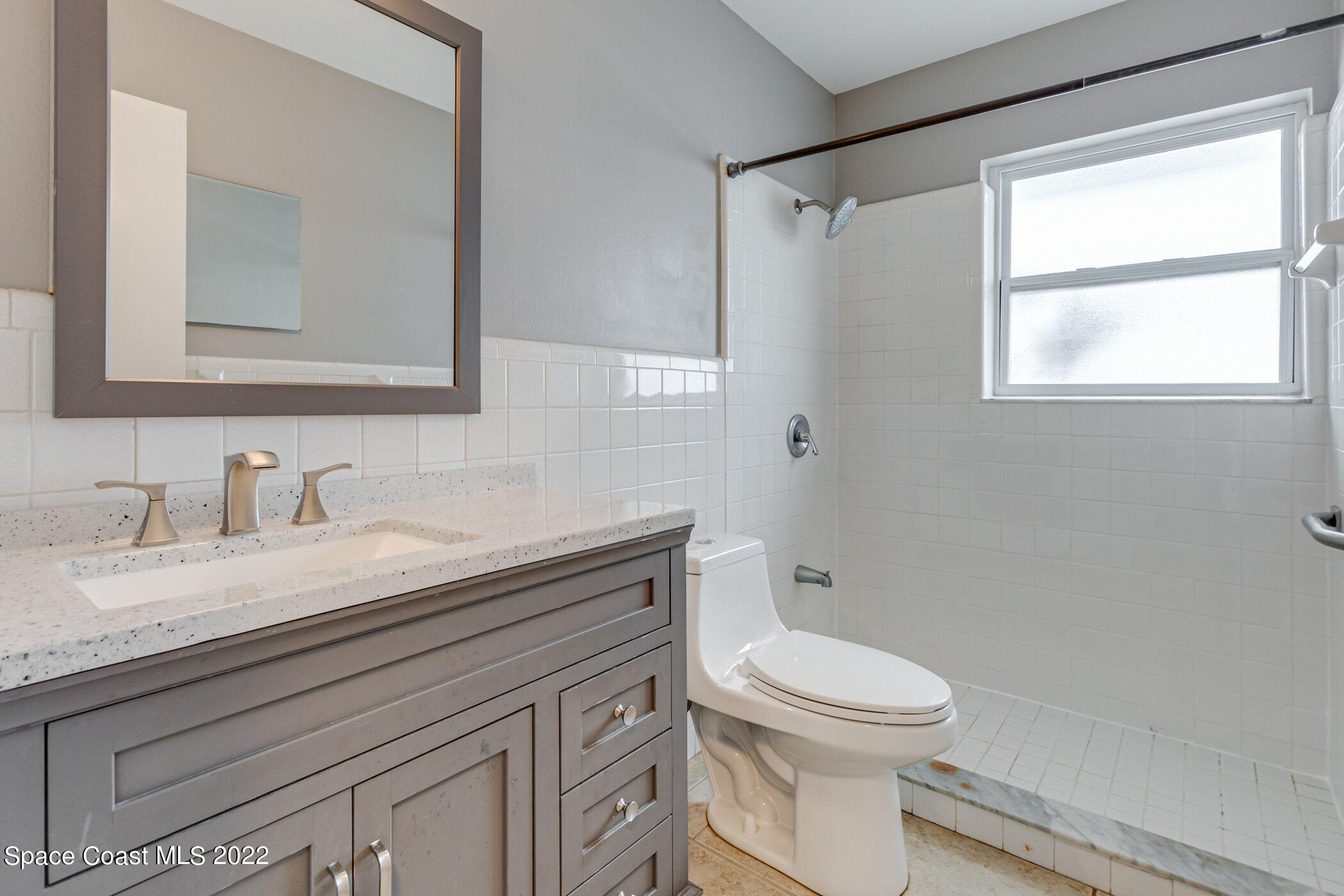 714 Catalina Road, Unit 9 Cocoa Beach, FL 32931 - Photo 14 of 33 a bathroom with a granite countertop sink toilet a large mirror and a window