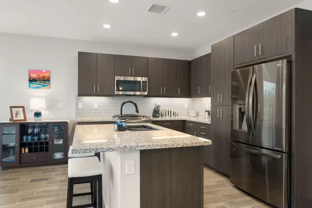 a kitchen with kitchen island granite countertop a refrigerator a sink a stove a dining table and chairs