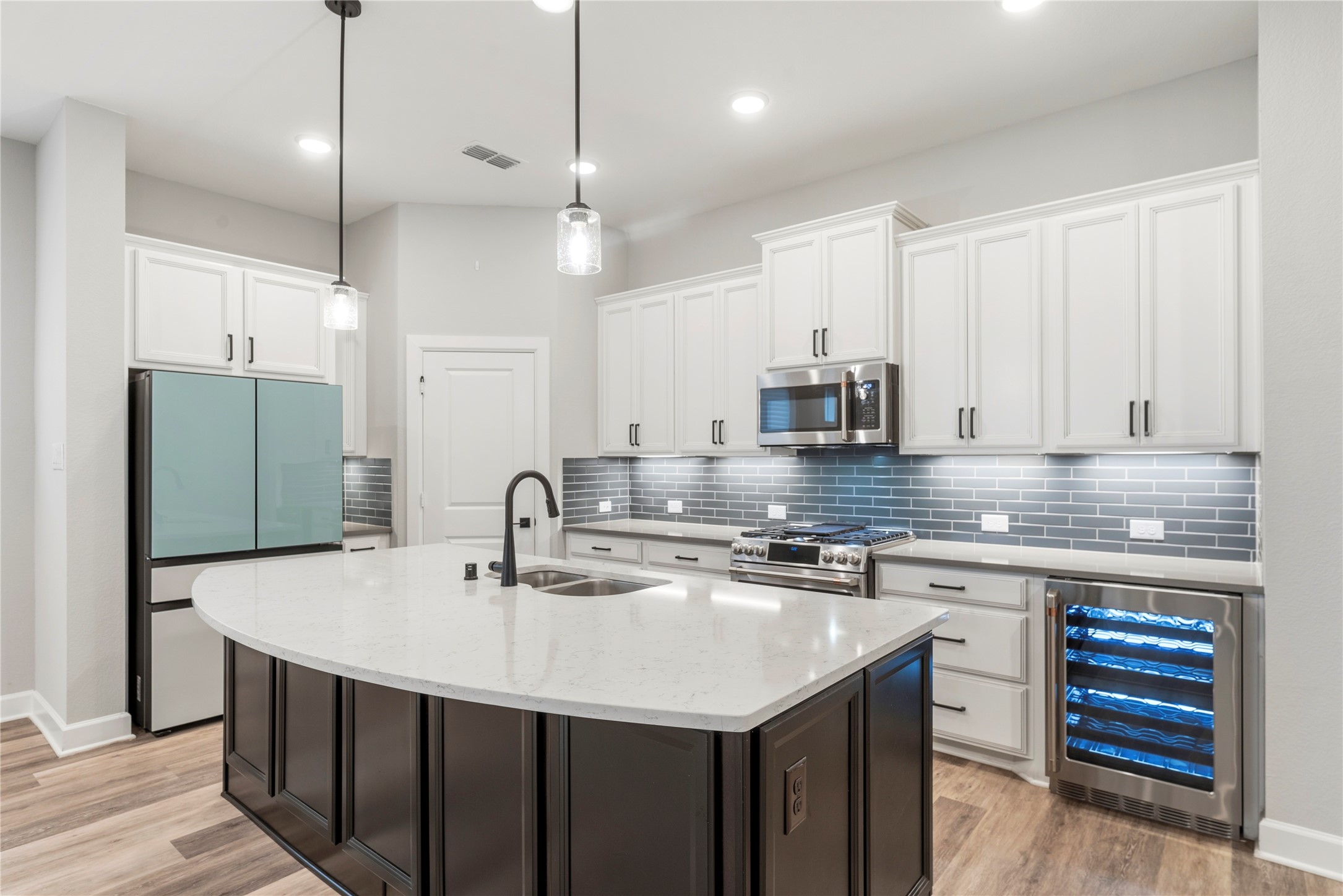 3438 Rich Radish Road Richmond, TX 77406 - Photo 5 of 25 The high-end, open-concept kitchen centers around a grand social island topped with premium Lyra quartz. The modern setup features Timberlake cabinetry with cushion-close technology, a sleek grey subway tile backsplash, and under-cabinet lighting.