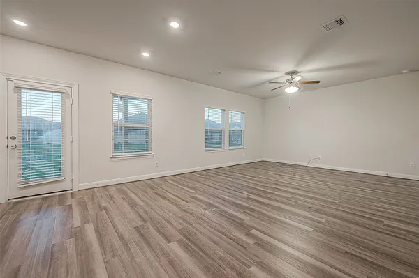 an empty room with wooden floor chandelier fan and windows