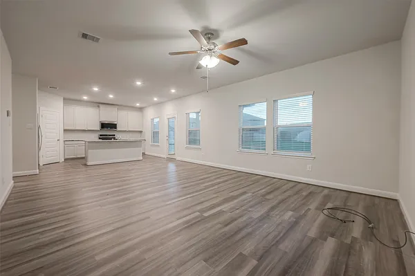 a view of an empty room with wooden floor and a kitchen