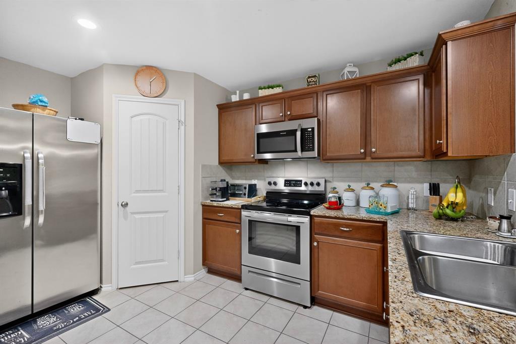 1409 Slate Street Princeton, TX 75407 - Photo 10 of 36 Kitchen featuring stainless steel appliances, granite-style countertops, wood cabinetry, tile flooring, and a tile backsplash