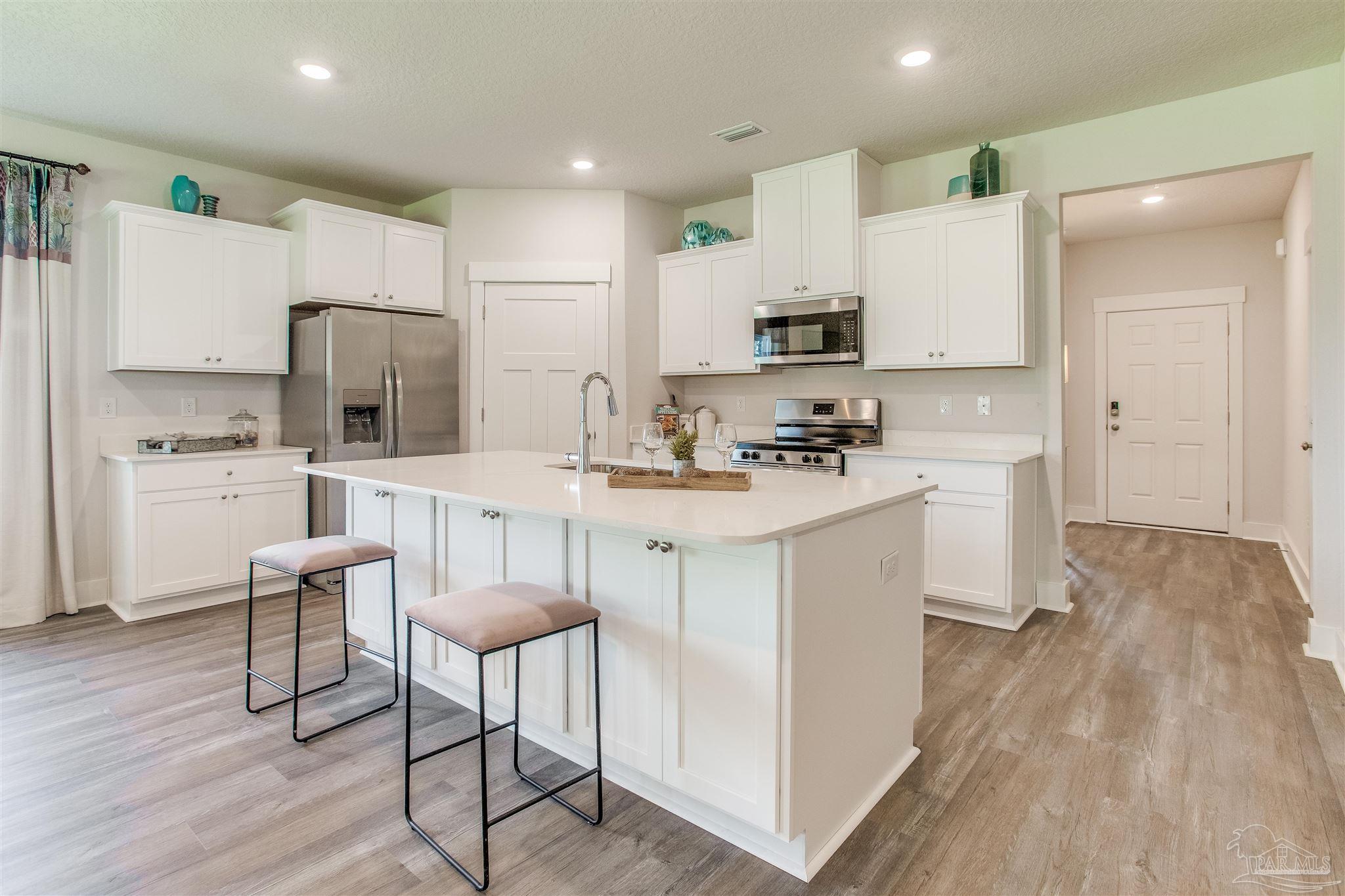 3452 Serviceberry Road Cantonment, FL 32533 - Photo 5 of 38 a kitchen with a sink a refrigerator and white cabinets with wooden floor