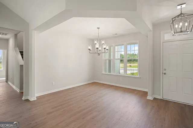 an empty room with wooden floor chandelier and windows