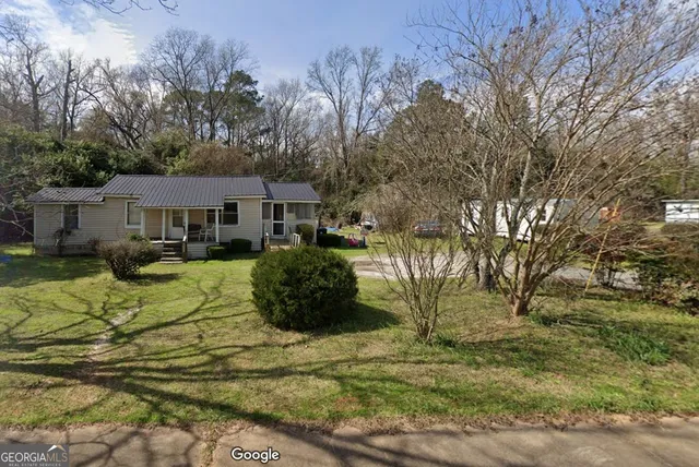a view of a white house next to a yard with a large tree