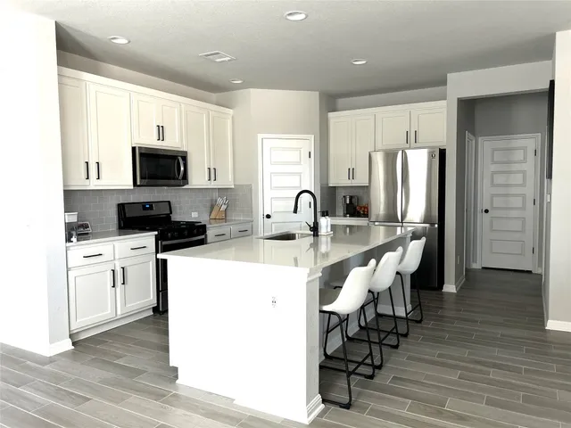 a kitchen with stainless steel appliances a microwave a sink a stove a refrigerator cabinets and a dining table