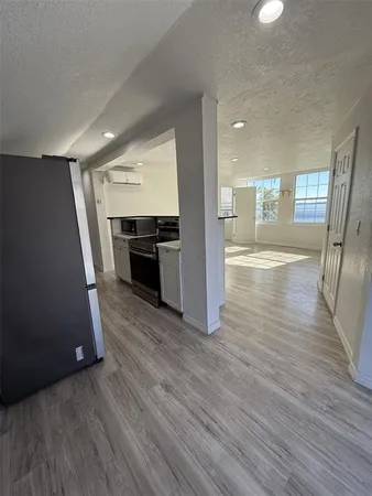 an empty room with wooden floor kitchen view and windows