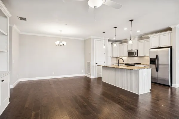 a kitchen with stainless steel appliances granite countertop a refrigerator a sink dishwasher a stove and white cabinets with wooden floor