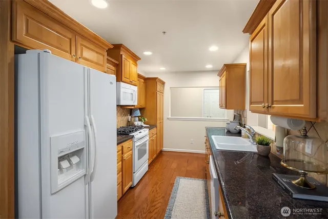 a kitchen with stainless steel appliances granite countertop a refrigerator a stove and a sink with wooden floor