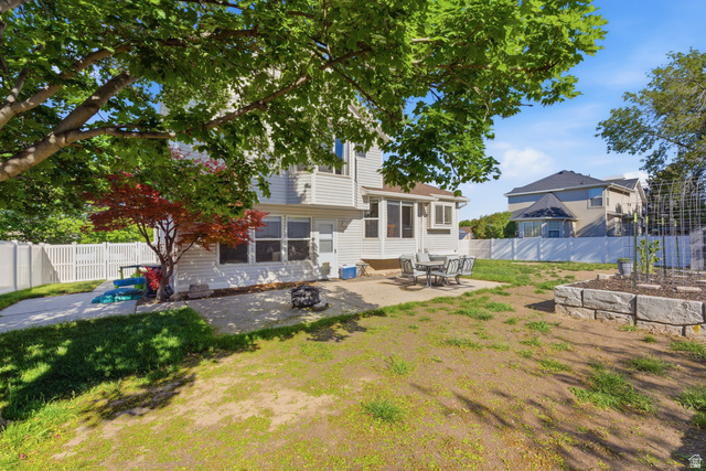 11189 Ohenry Road East Sandy, UT 84070 - Photo 31 of 44 Expansive backyard featuring a partial concrete patio, white vinyl fencing, a raised garden bed with stone retaining walls, and a prominent mature tree with a small red-leafed tree