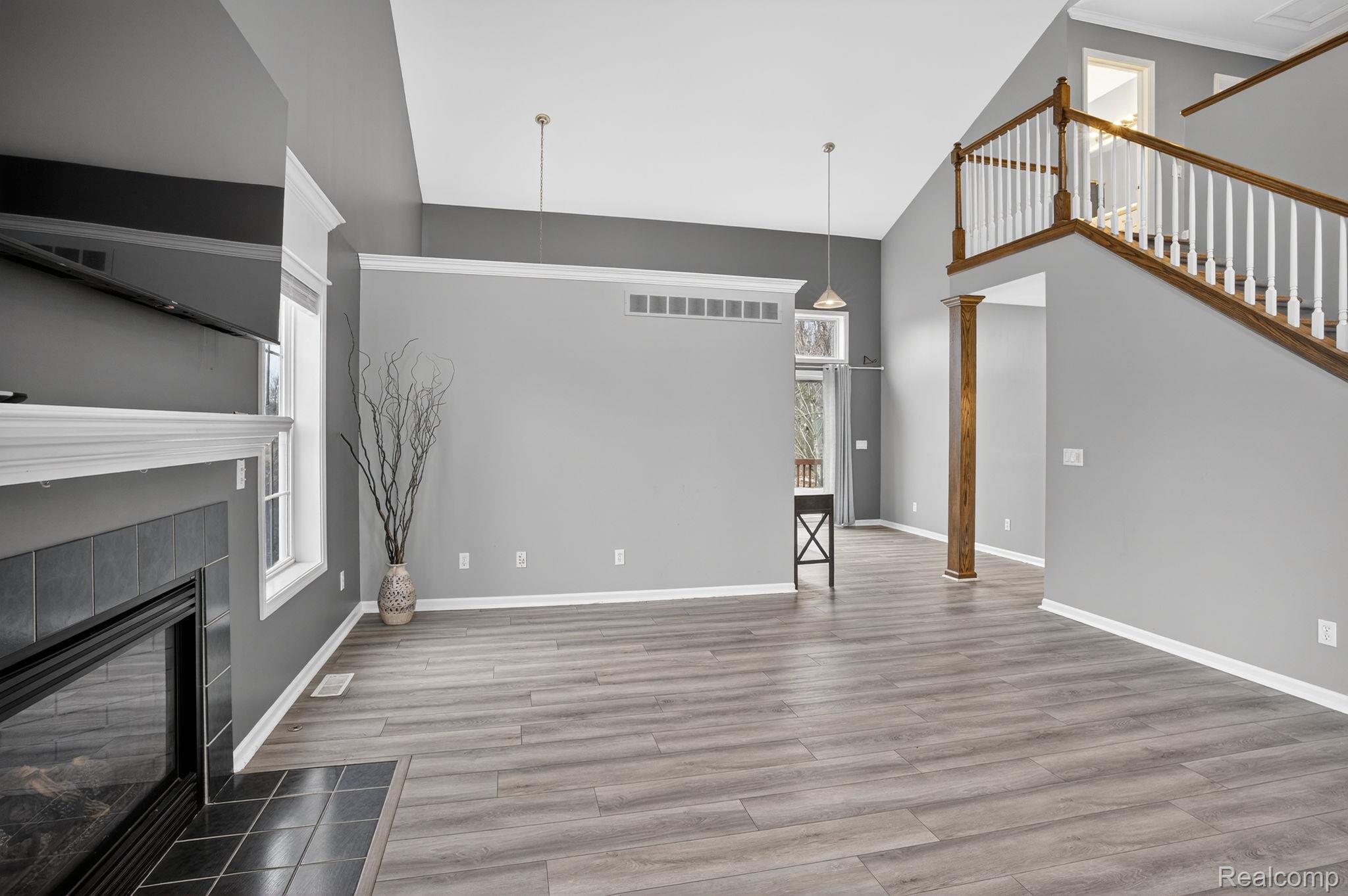 9055 Hegel Road Grand Blanc, MI 48439 - Photo 20 of 62 Spacious living area featuring vaulted ceilings, wood-finish flooring, a tile-surround fireplace with mantel, and an open staircase with wood handrails and white balusters