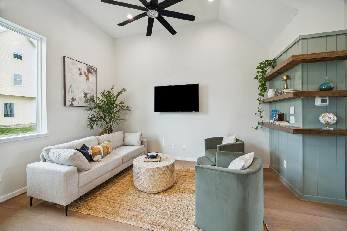 3903 Yale Street Houston, TX 77018 - Photo 15 of 45 A bright, modern living room with a beige sectional sofa and green armchairs around a round coffee table. A black ceiling fan and wall-mounted TV add contemporary touches. Minimal decor and a potted plant create an inviting, airy atmosphere, enhanced by natural light from a side window.