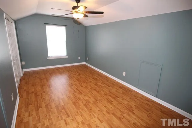 an empty room with wooden floor fan and windows