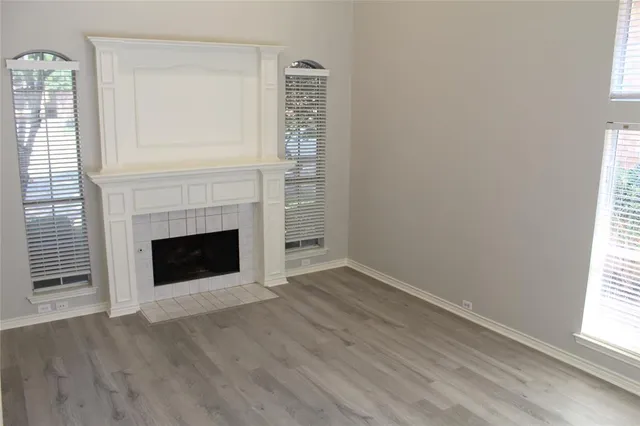 an empty room with wooden floor fireplace and windows