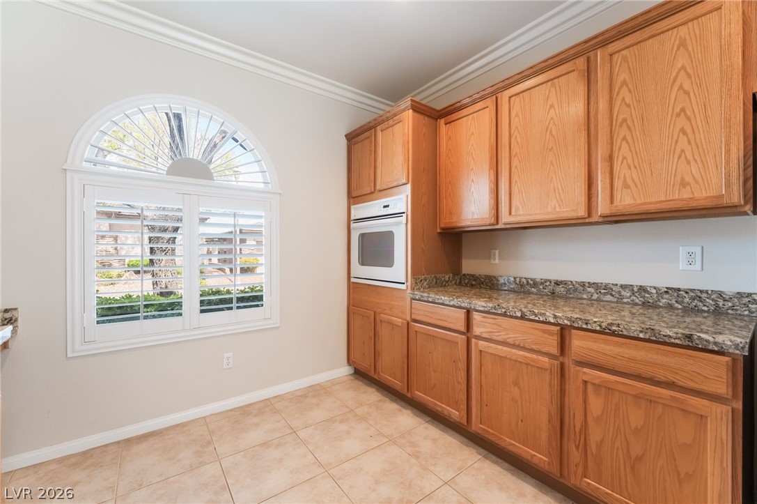 10481 Riverside Park Avenue Las Vegas, NV 89135 - Photo 13 of 51 Kitchen featuring oven, crown molding, dark stone countertops, wood finish cabinets, and light tile patterned floors
