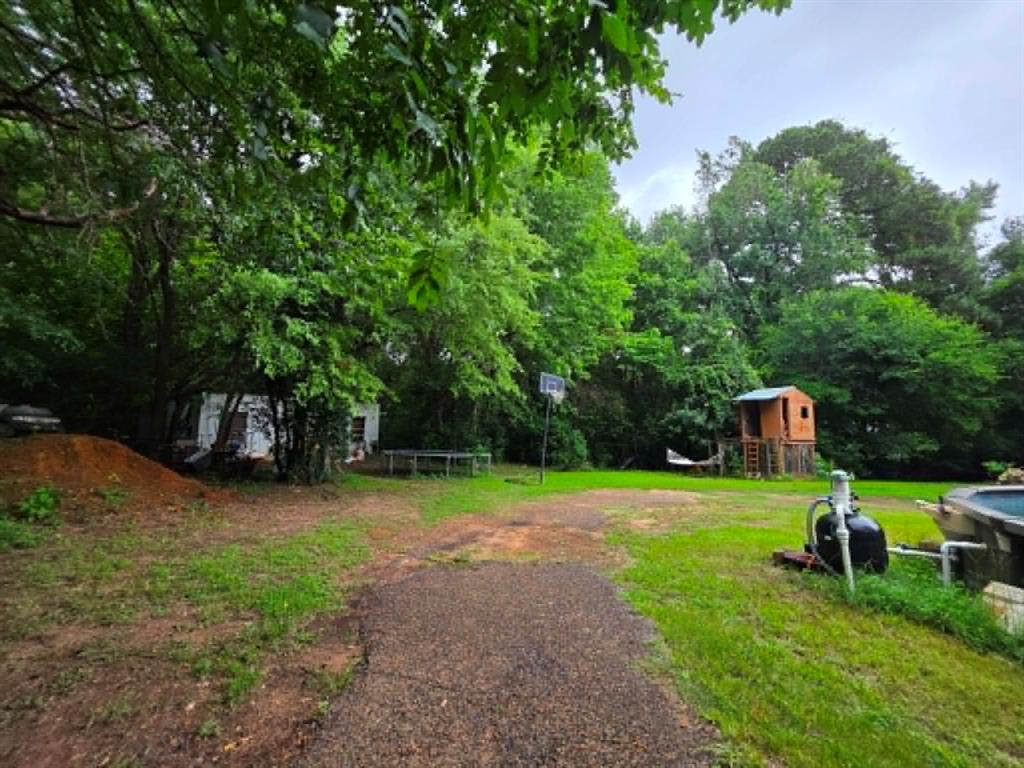 4514 West Loop 281 Longview, TX 75604 - Photo 11 of 36 Expansive rear yard featuring a gravel pathway, mature trees, a detached storage building, and a built-in playhouse structure