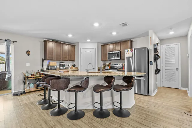 a kitchen with stainless steel appliances kitchen island granite countertop a refrigerator a stove a sink and a dining table with wooden floor