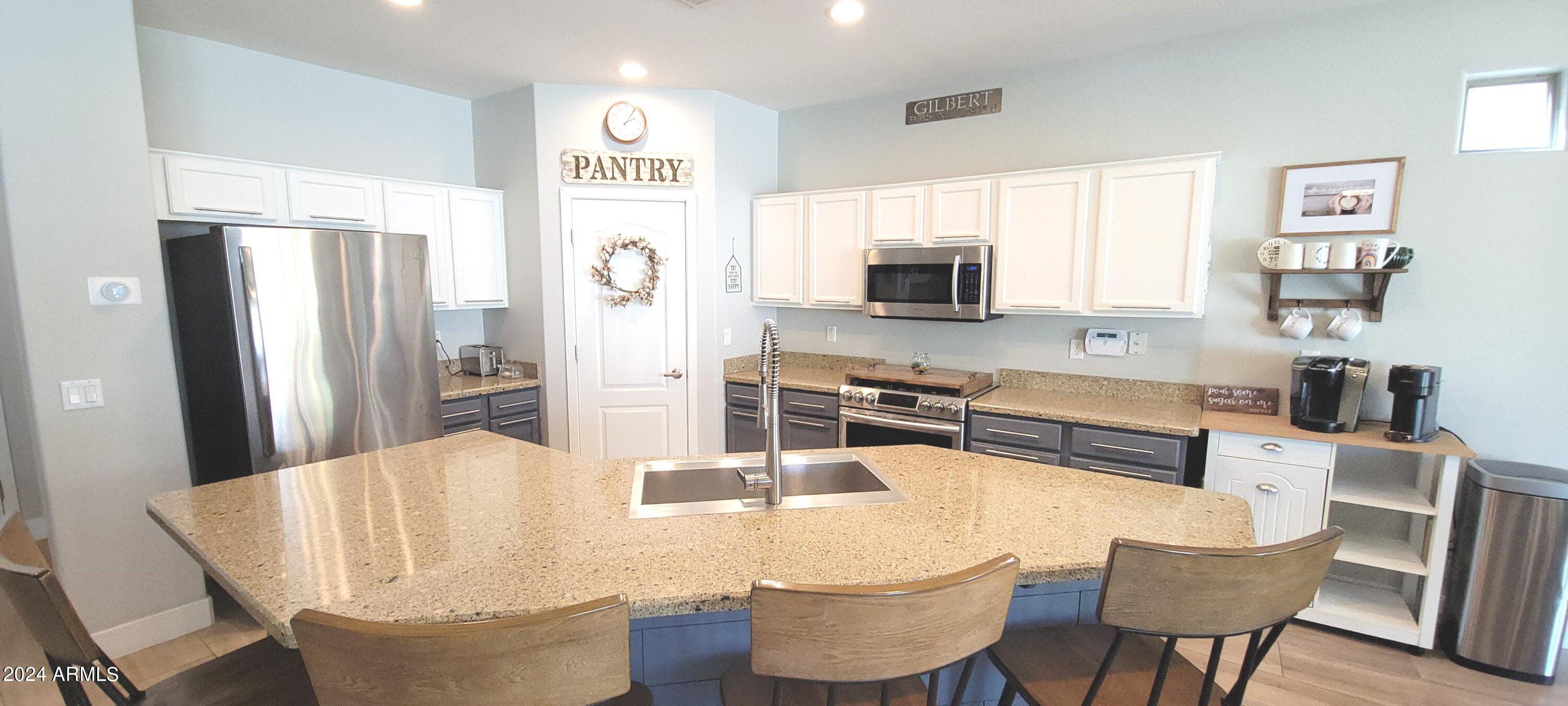 3236 East Phelps Street Gilbert, AZ 85295 - Photo 21 of 50 a kitchen with stainless steel appliances kitchen island granite countertop a refrigerator a stove a sink dishwasher and white cabinets with wooden floor